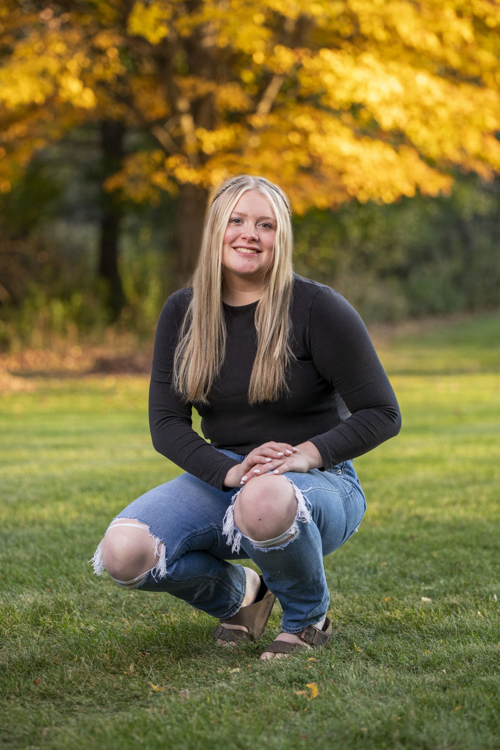 Arrowhead senior crouching with fall leaves behind her. 