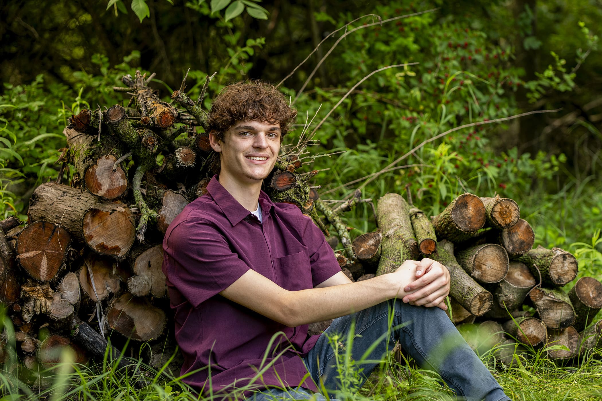Arrowhead senior sitting against wood pile.