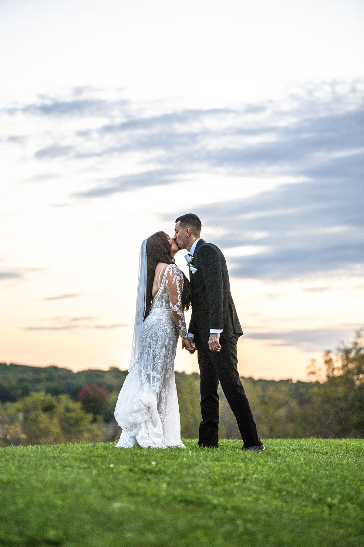 Bride and groom kissing in field at sunset 
