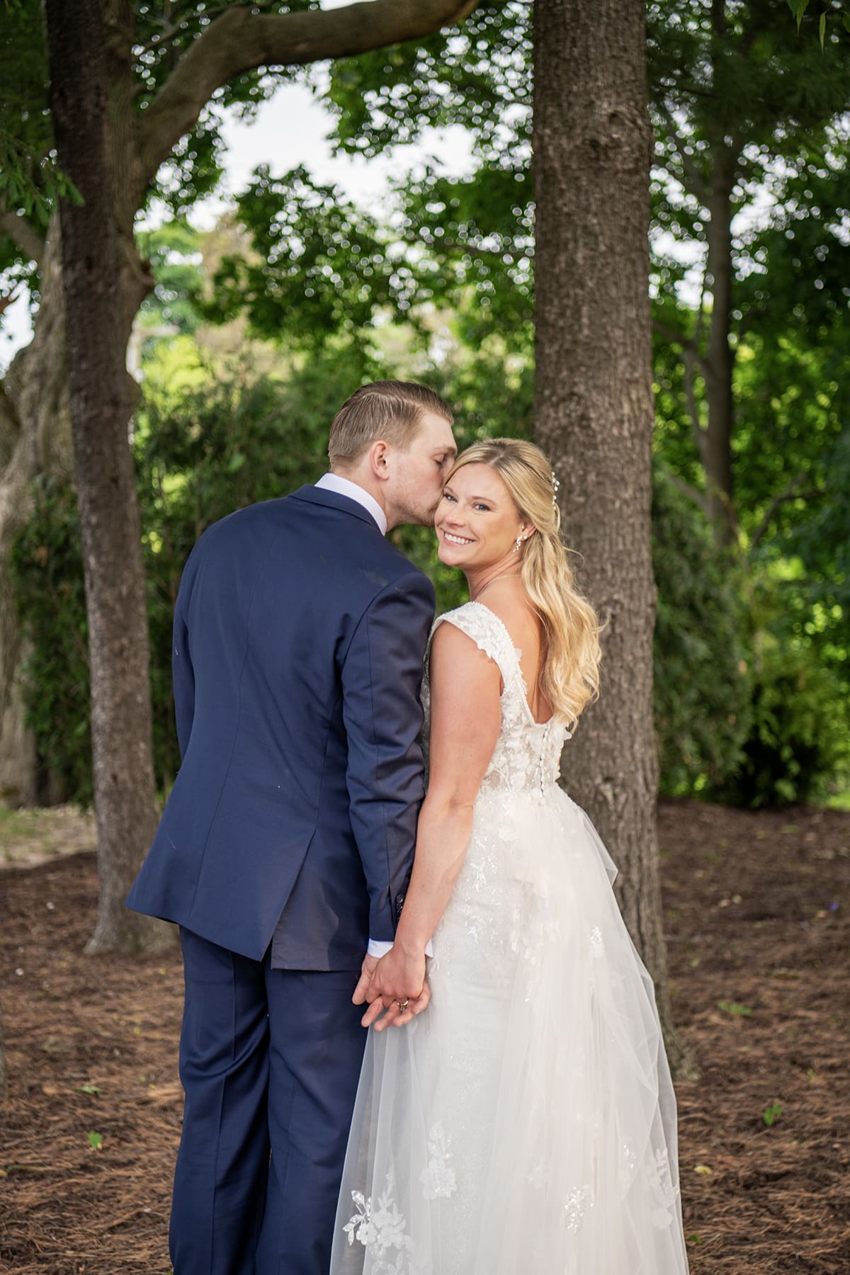 Groom kissing bride as she smiles at camera 