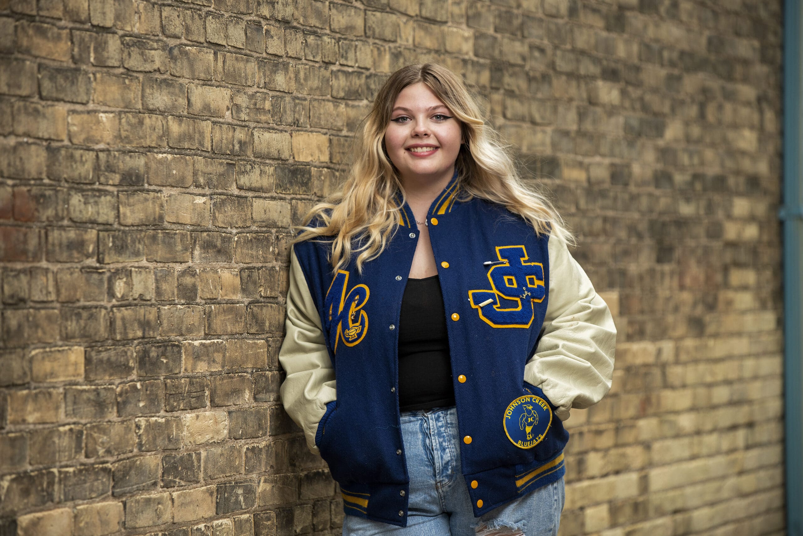Delafield senior leaning against wall with her letterman jacket on.