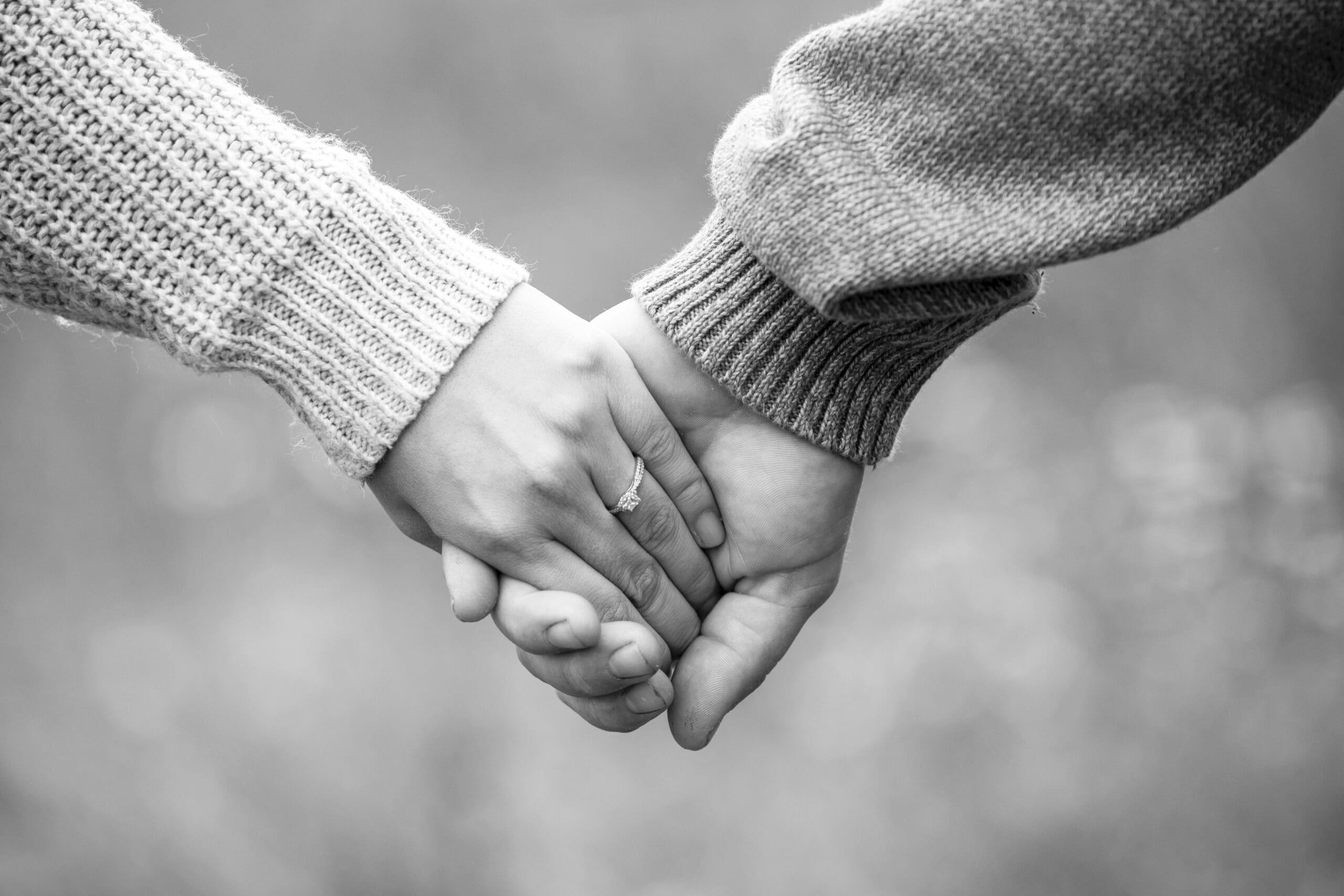 Detail shot of engagement ring while couple holds hands.