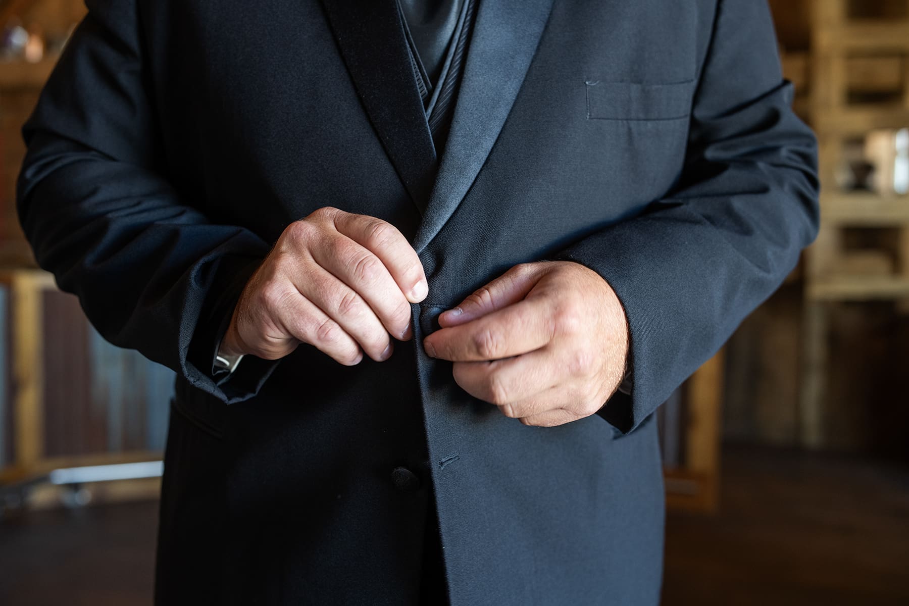 Detail of groom's hands buttoning his suit as he gets ready
