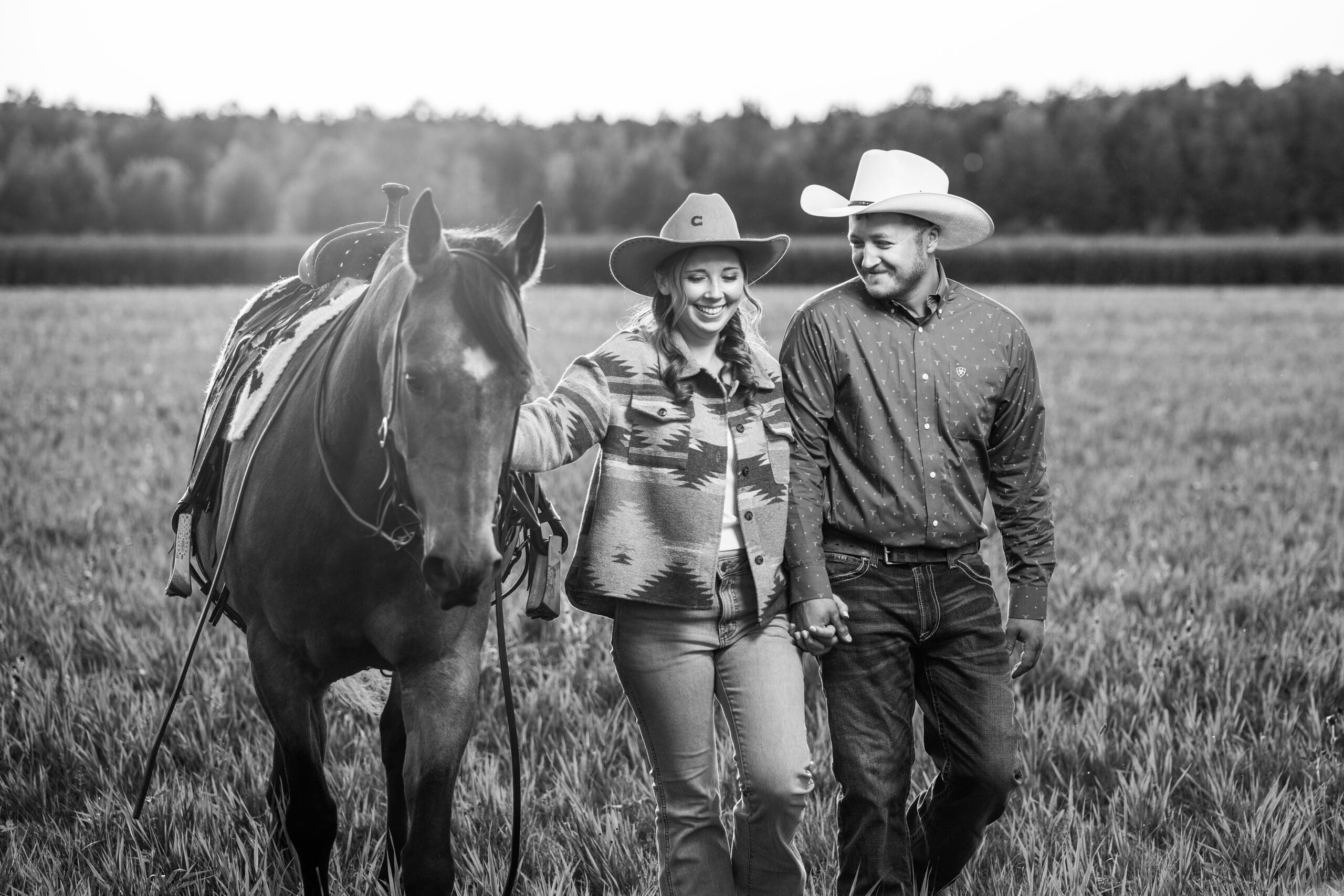 Engaged couple walking through field with their horses in Hartland