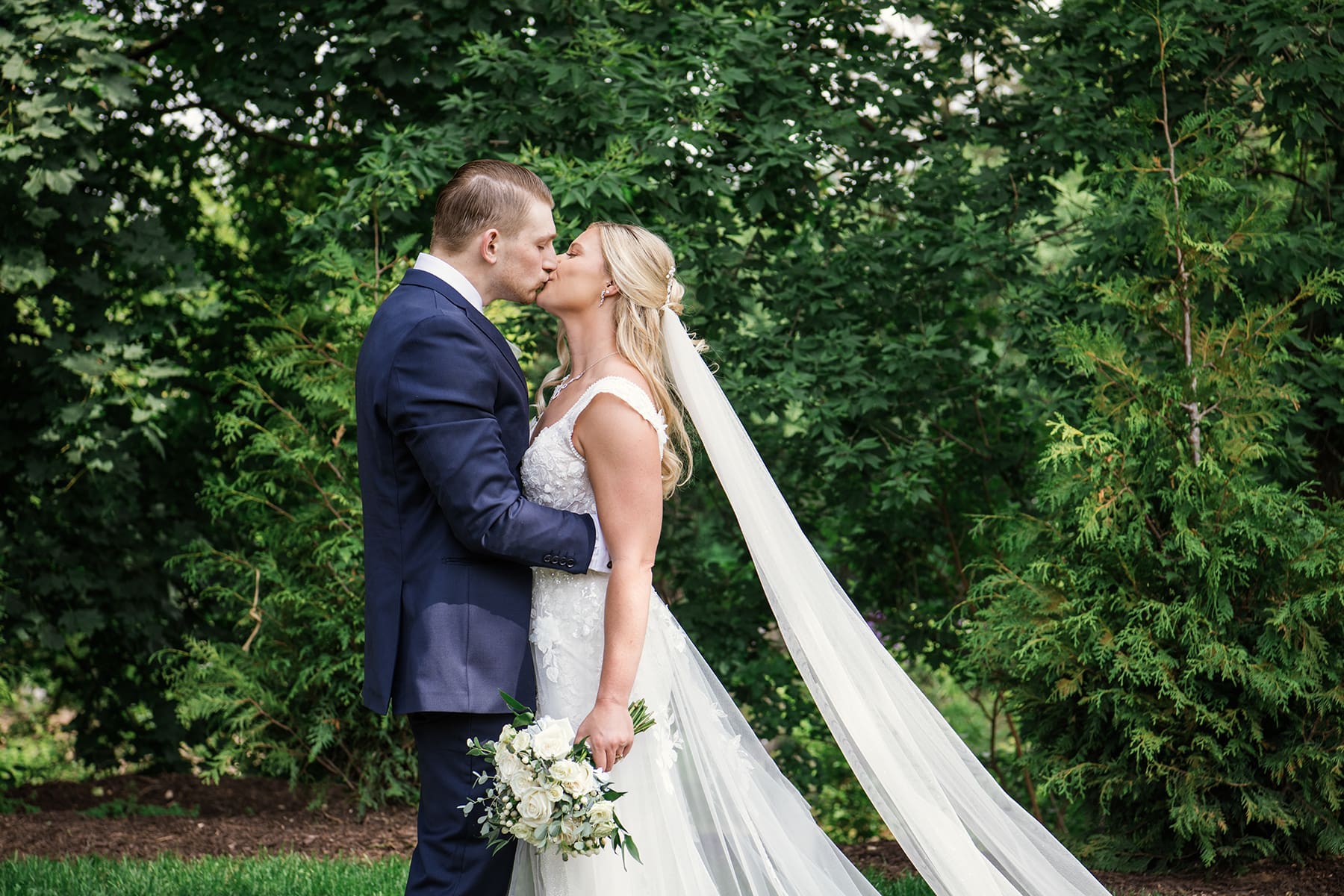 Groom kissing bride while surrounded by Wisconsin greenery 