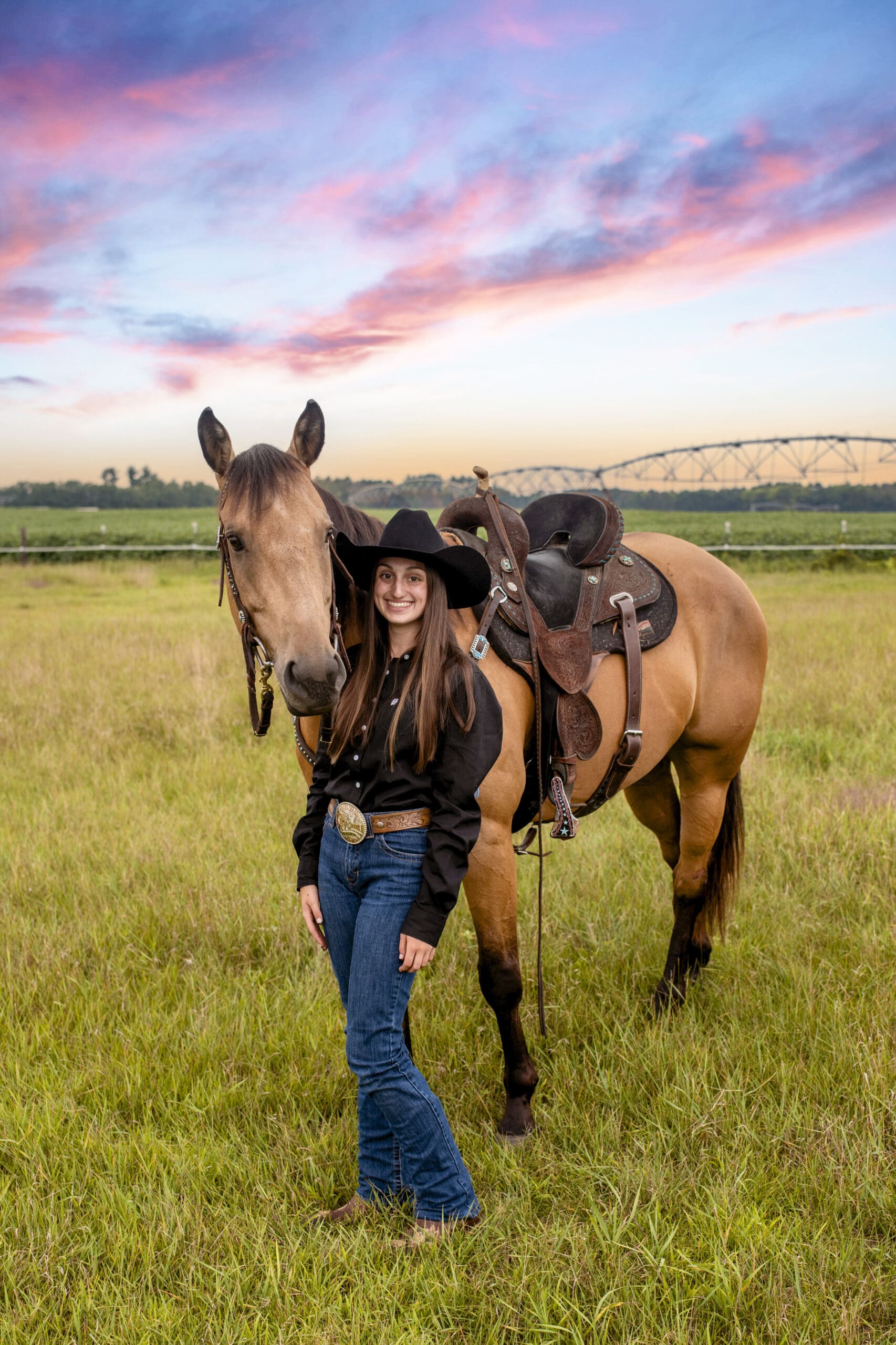 Hartland senior standing by her horse at sunset in a field.
