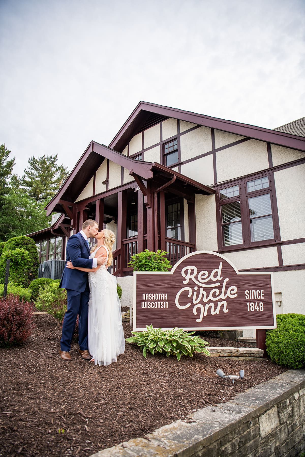 Bride and groom kissing by Red Circle Inn sign 