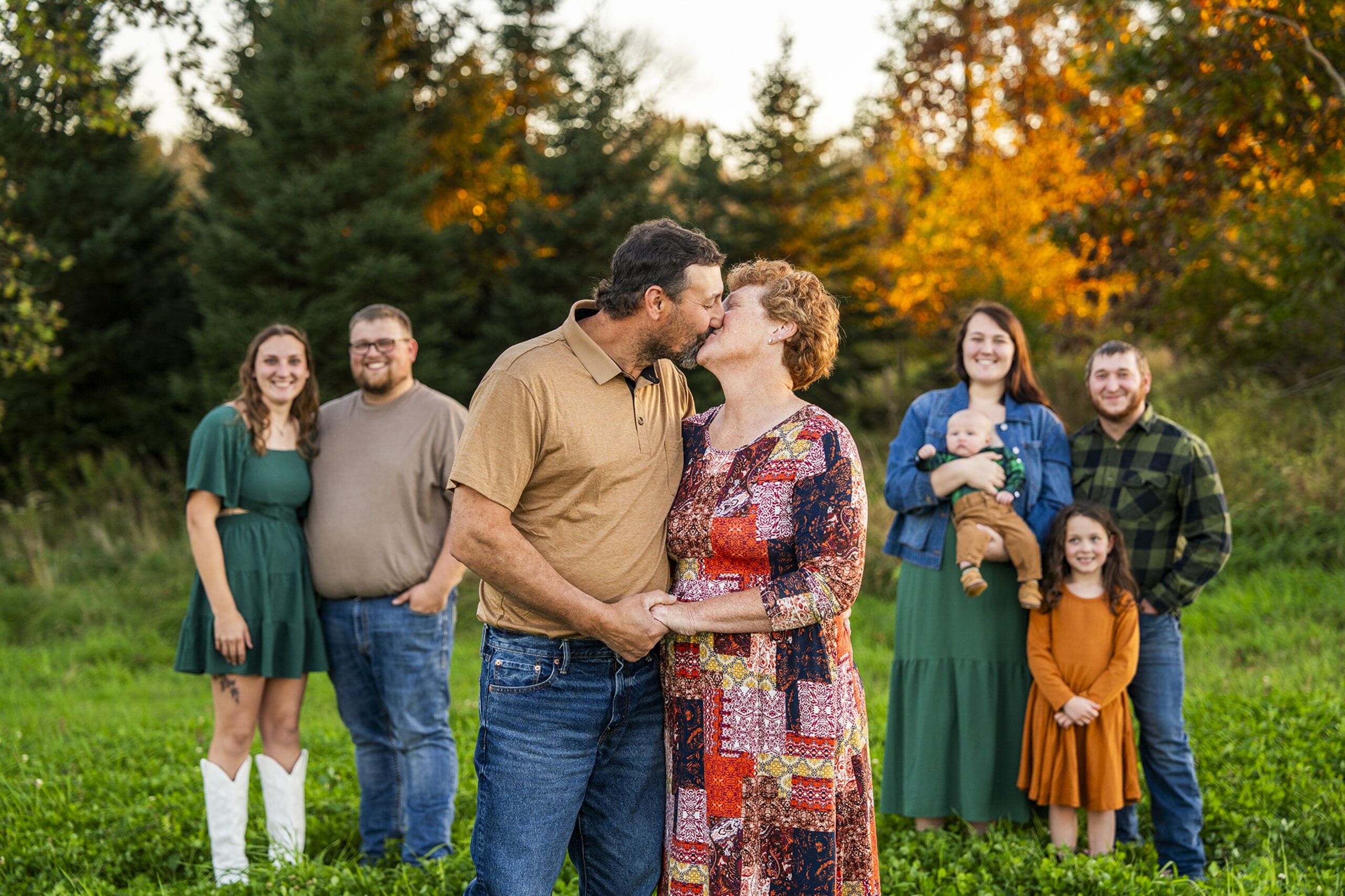 Delafield parents kissing during family photo session while children stand behind them.