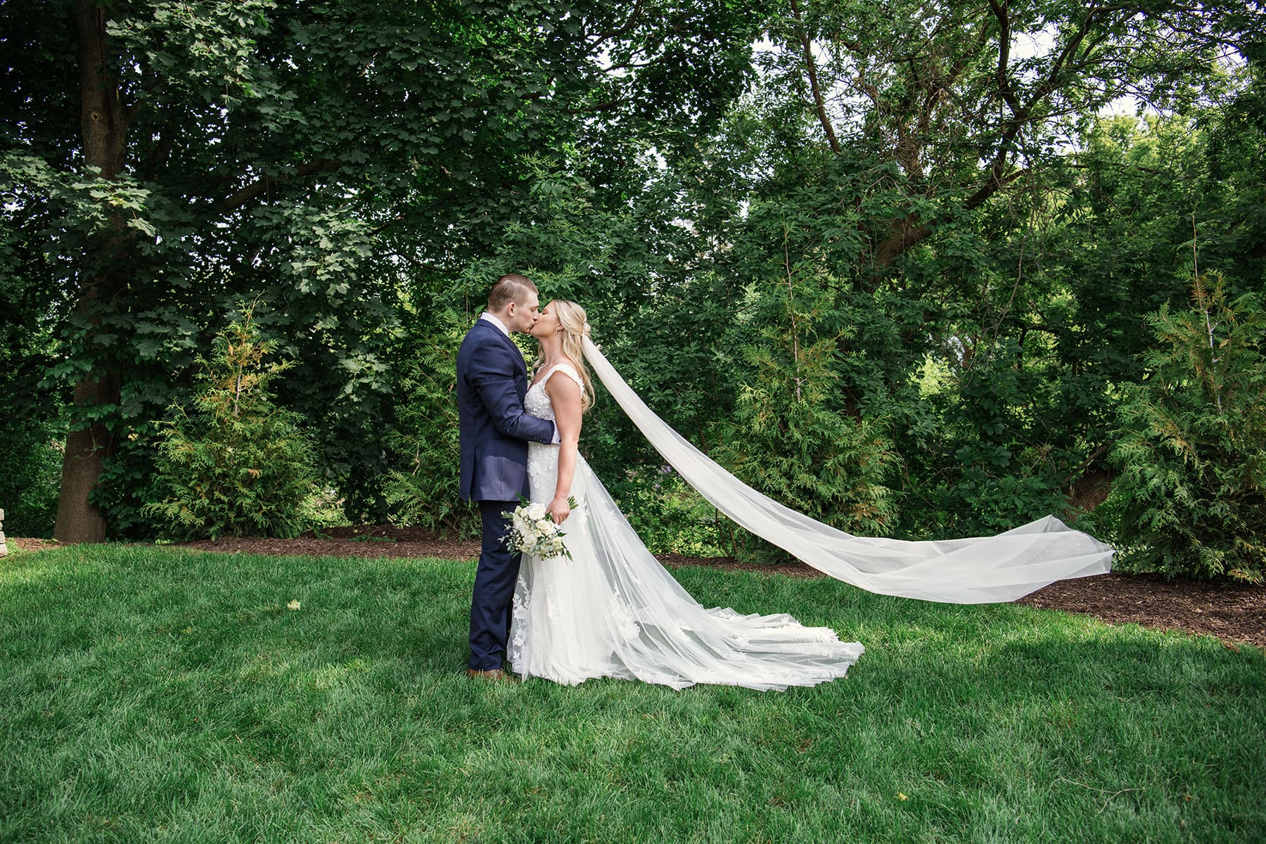 Wide view of groom and bride kissing with her veil blowing in the wind